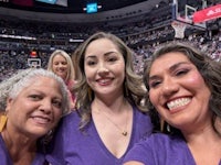 three women in purple shirts posing for a photo at a basketball game